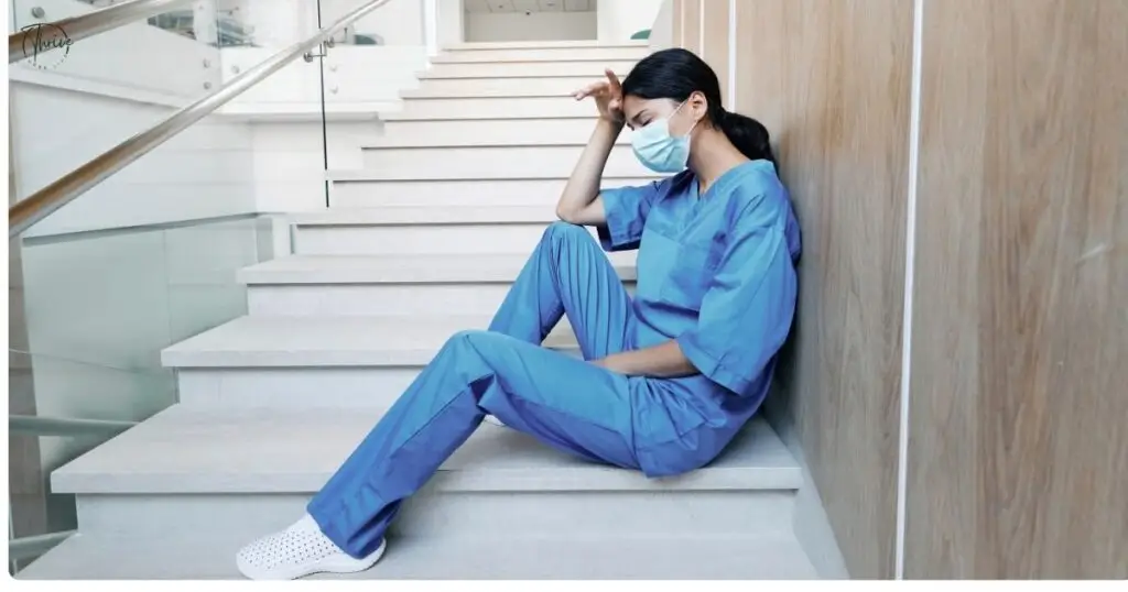 A nurse sitting in a hospital stairwell, eyes closed and breathing deeply.