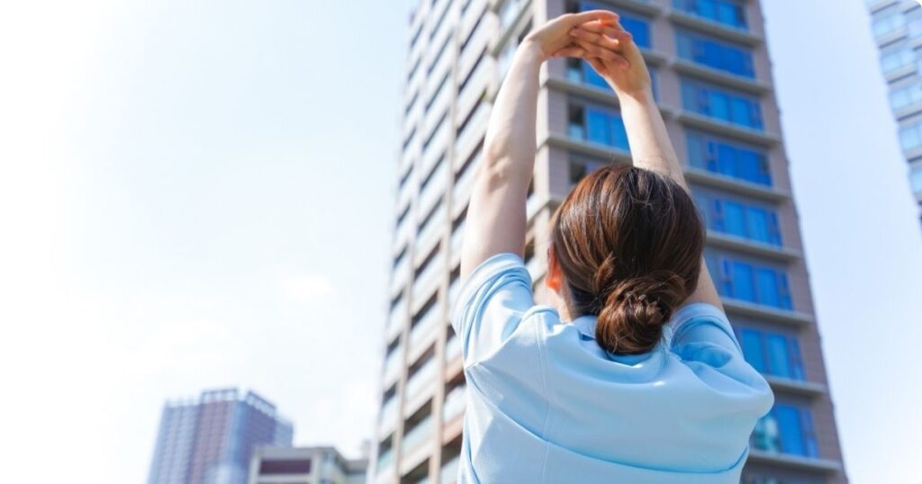 A young nurse in scrubs is stretching her arms overhead– a quick strength training for nurses routine.